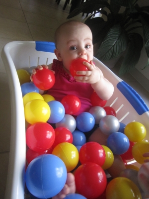 Evie sitting in a clothes basket full multi-coloured plastic balls